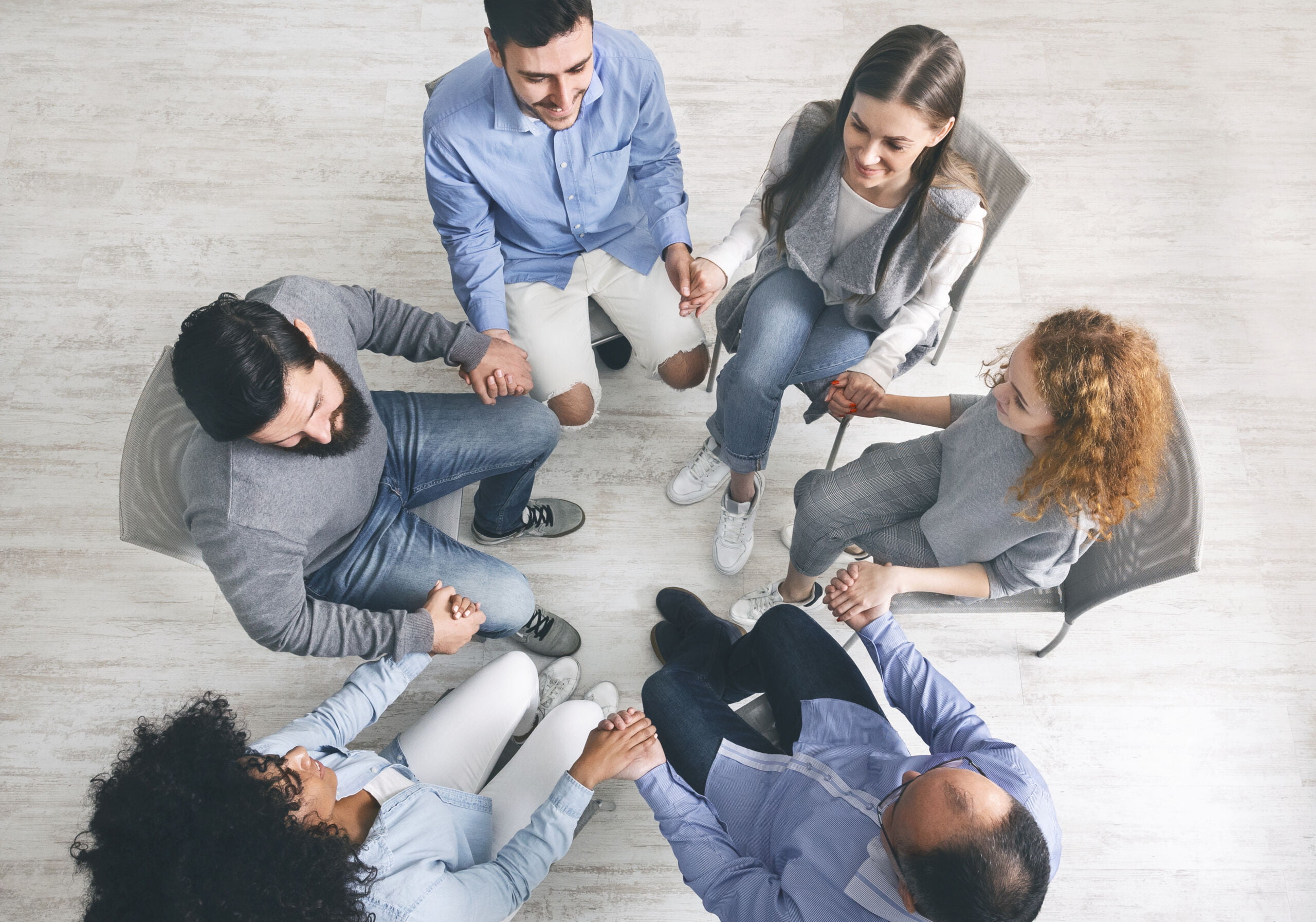 Diverse group of individuals participating in a therapy session, sitting in a circle and holding hands, symbolizing support and understanding.